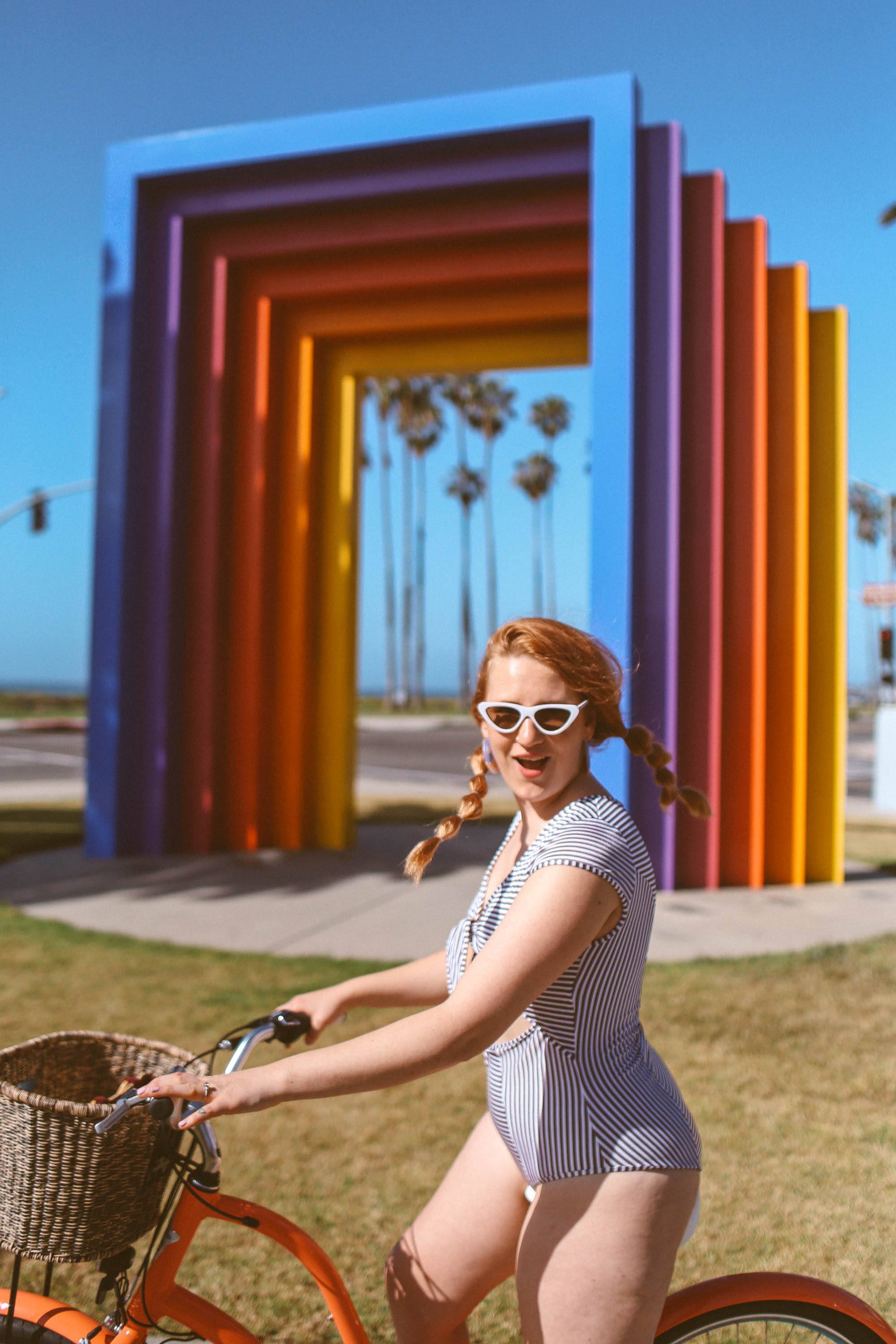 Woman in black and white striped front tie swimsuit riding a bike at the chromatic gate in Santa Barbara