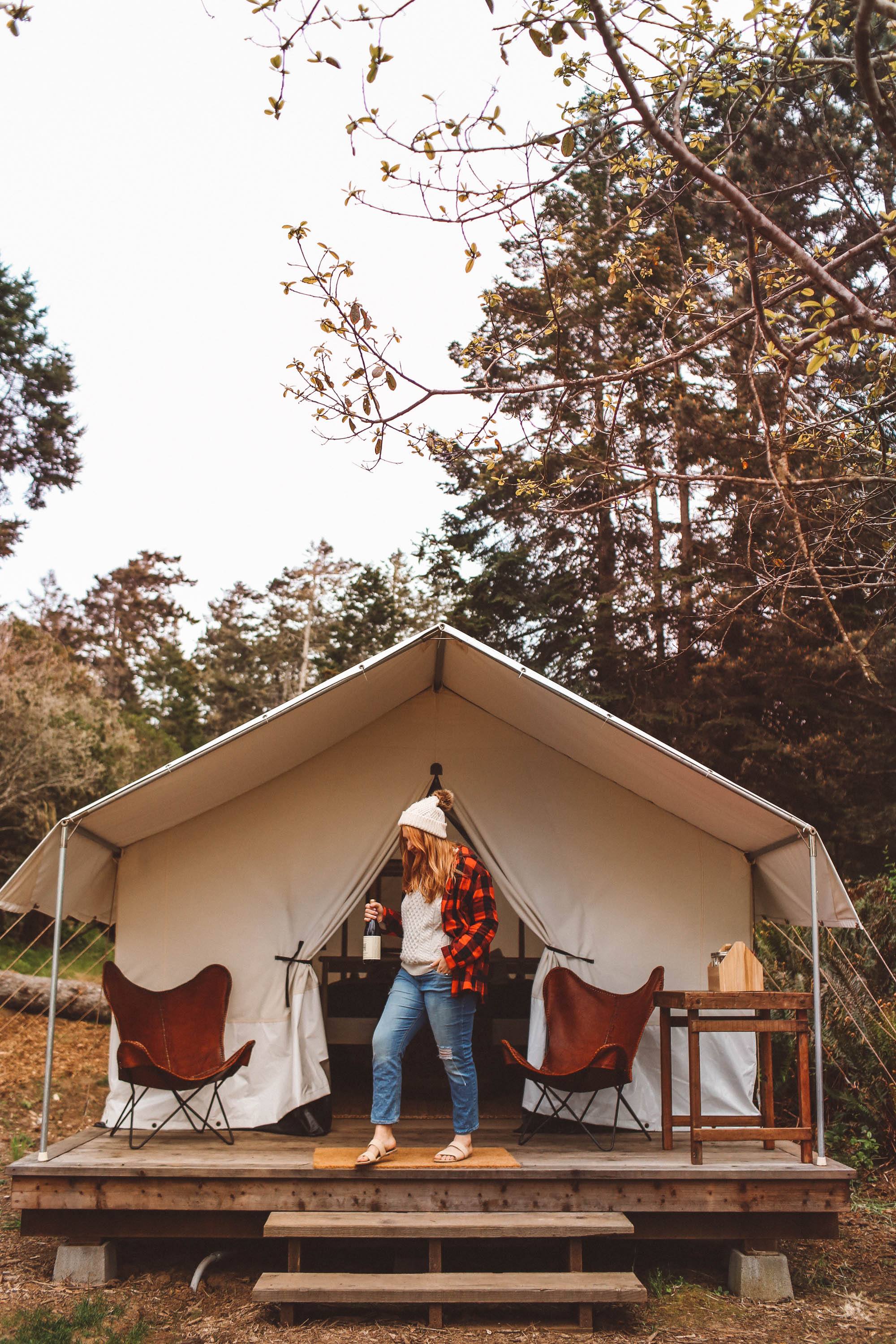 Woman standing on wood porch with wine in front of a tent