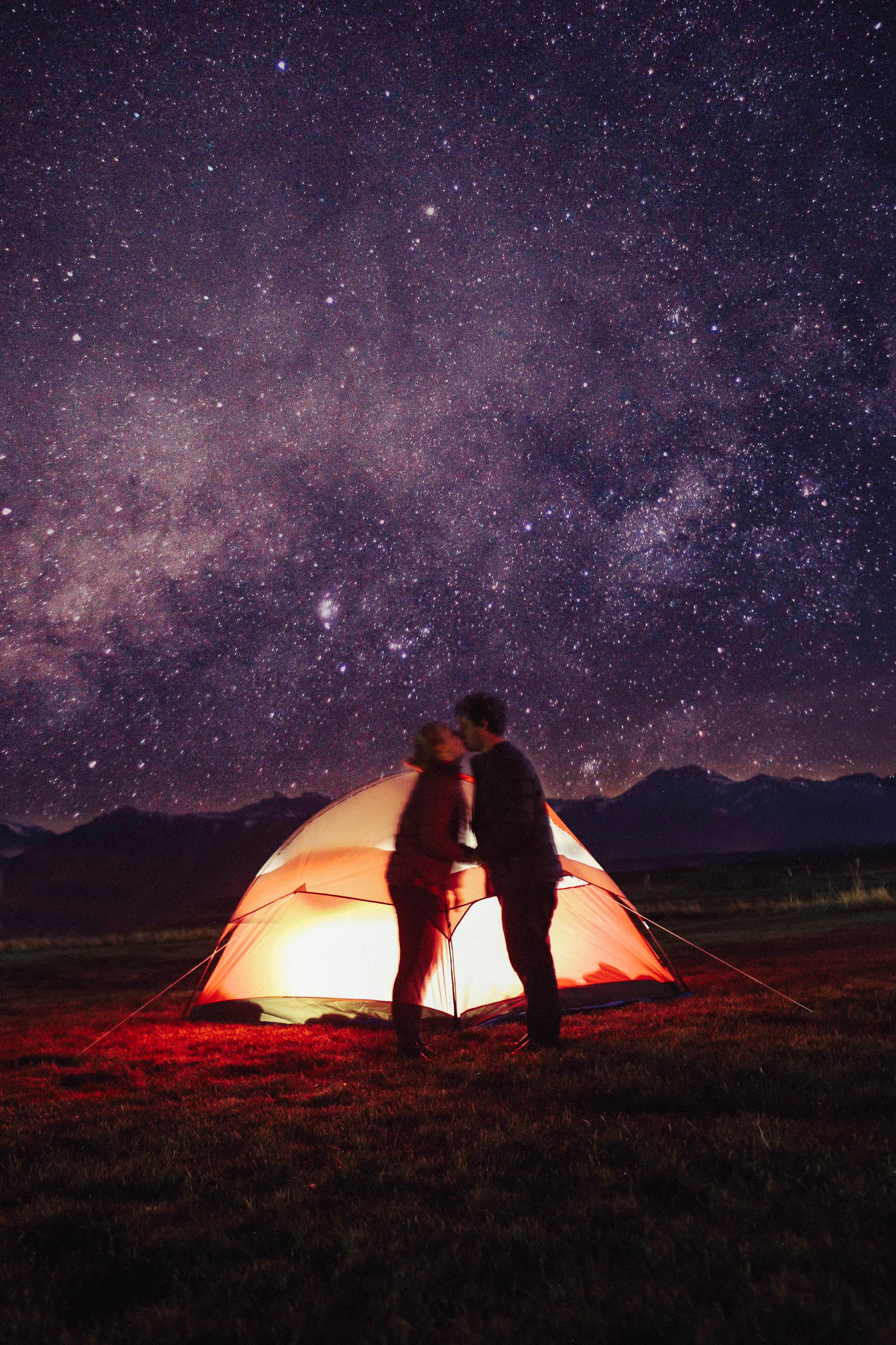 people kissing in front of a glowing tent on a starry night