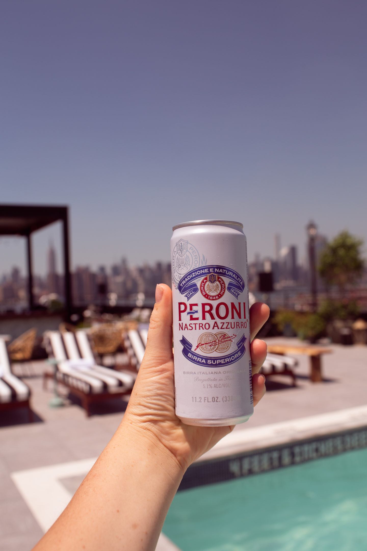 hand holding a beer at a rooftop pool in Brooklyn